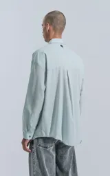 Camisa manga larga verde agua con bolsillo en el pecho, de calce oversize confeccionada en textil plano fresco y liviano.