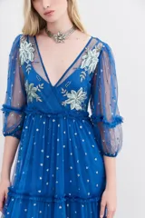 Vestido largo de tul bordado color azul con hilo de lurex y lentejuelas plateadas. Tiene escote en V cruzado, mangas 3/4 con volados y puños elásticos, frunces en la cintura y viso a tono.