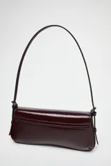 Bolso de hombro color borgoña con efecto acharolado, solapa con cierre magnético y asa ajustable.