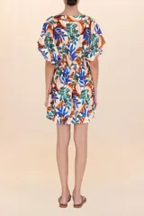 Vestido corto de manga mariposa, escote en V y cintura ajustada con frunce. Presenta un estampado botánico vibrante sobre fondo blanco, con hojas en tonos azules, naranjas y verdes.