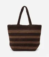 Bolso de playa tipo tote, confeccionado en paja color marrón con rayas horizontales negras.