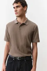 Remera polo marrón en punto texturizado de peso medio, de manga corta con cuello, tapeta de botones y bajo recto. Corte ajustado que realza el contorno del cuerpo creando una silueta entallada.