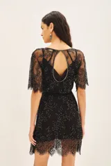 Vestido corto negro con mangas cortas de encaje, bordado a mano con mostacillas y lentejuelas. Presenta escote en U con abertura en forma de gota en el centro del busto, ribeteado con mostacillas. Incluye un cinturón bordado y un forro interior con breteles regulables.