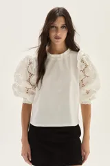 Blusa blanca de algodón con mangas abullonadas de broderie con diseño floreado. Presenta volados en el cuello y hombros, con un estilo romántico y femenino.