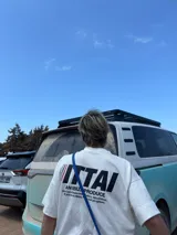 Remera color crema de corte recto y mangas cortas, con estampado en la espalda con el logo "ITTAI" en negro con líneas rojas, azules y blancas, y la leyenda "AN IBIZA PRODUCE. Ittai Stars Department Gallery - Ibiza Edition. If you're in Ibiza, 112 is not an option.".