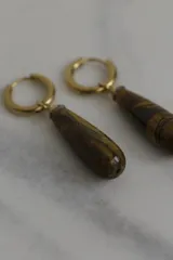 Par de aros colgantes con argolla dorada y dije en forma de gota de piedra natural color marrón con vetas negras.