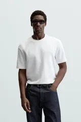 Camiseta blanca de algodón interlock con elasticidad, corte recto, cuello redondo y mangas cortas.
