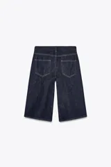 Bermuda de jean azul oscuro, tiro medio, con cinco bolsillos, trabillas en la cintura y pespuntes marcados a contraste.