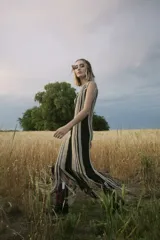 Vestido largo tejido al crochet con lurex, con diseño a rayas verticales en tonos beige y negro, y terminación con flecos.