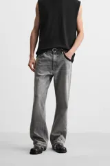 Pantalón de jean negro con efecto lavado, corte flare, cinco bolsillos, cierre frontal con cremallera y botón, y bajo con acabado irregular.