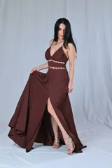 Vestido largo de fiesta color marrón chocolate, con breteles finos, escote en V y tajo lateral. Presenta detalle de doble abertura en la cintura con apliques de argollas doradas.