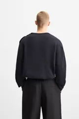Sweater negro de punto con estructura de canalé, corte relaxed fit, cuello redondo y cierre de botones en el hombro.