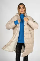 Campera puffer larga color beige, con cuello alto y cierre frontal con botones a presión. Tiene bolsillos laterales y un parche con el logo de la marca en la manga izquierda.