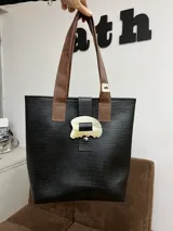 Bolso tipo tote bag negro con textura símil cuero de cocodrilo, doble asa corta de cuero marrón y beige, y cierre con broche metálico con forma orgánica.