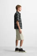 Camisa de hombre relaxed fit con estampado de cuadros blancos sobre fondo negro, cuello solapa, manga corta y cierre frontal con botones.
