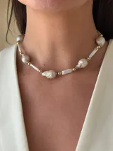 Collar corto de perlas de río alargadas y ovaladas, con cuentas de acero quirúrgico y bolitas con baño de oro. Cierre con cadena de acero quirúrgico y gancho para regular el largo.