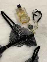 Conjunto de lencería de encaje negro con blanco, compuesto por un corpiño triangular con breteles regulables y cierre de gancho delantero, y una tanga regulable.