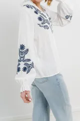 Camisa de manga larga en algodón liviano, color azul marino, con bordados florales en contraste en el frente y mangas. Cuello mao con terminación en ondas y puños fruncidos.