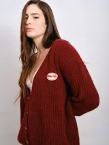 Cardigan marrón de punto grueso con cuello en V, cierre frontal con botones y parche bordado en el pecho.