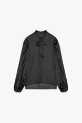 Camisa fluida negra de cuello redondo con lazada, manga larga tipo globo con pliegues en hombro y cierre frontal con botones ocultos por solapa.