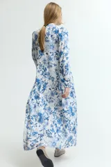 Vestido largo blanco con estampado floral en tonos azules. Tiene cuello mao, botones ocultos en la parte delantera, mangas largas abullonadas con puños elásticos, cinturón fino extraíble y costura fruncida debajo de la cadera para dar vuelo.
