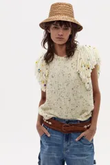 Chaleco tejido plano color crudo, sin mangas, con flecos bordados a mano en los hombros.