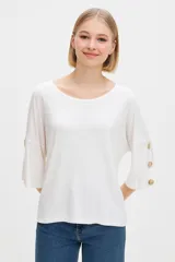 Remera blanca de manga 3/4, holgada, con cuello redondo y botones decorativos en las mangas.