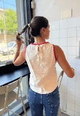 Chaleco sin mangas color blanco roto, con bordado de corazón anatómico en rojo en el pecho. Los bordes del cuello y las sisas tienen un ribete festoneado en color rojo.