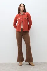 Chaqueta de tejido color terracota/lacre, con cuello y bordes de bolsillo en blanco con textura de punto. Posee cierre frontal de botones y manga larga.