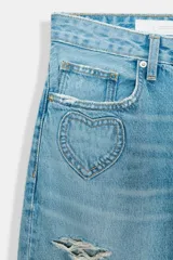 Jeans de denim celeste lavado, corte boyfriend ancho, tiro medio, con roturas y apliques/bordados en forma de corazón en diferentes partes de las piernas.