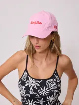 Gorra rosa de lona con visera, con bordado frontal de la marca Rusty Tribe en color rojo y logo bordado en el lateral.