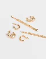 Set de tres pares de aros dorados: un par de aros largos con flechas colgantes, un par de aros tipo argolla lisa y un par de aros tipo argolla con strass.