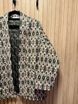 Chaqueta con estampado de arabescos en tonos marrones, beige y negro, con cuello mao, mangas largas y lazo para ajustar en la cintura.