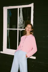 Chaqueta de punto rosa con cuello redondo y manga larga. Tiene bolsillos delanteros y cierre frontal con botones celestes.