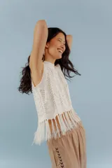 Chaleco de hilo color crema, con cuello redondo y diseño calado. Presenta flecos en el ruedo.