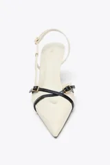 Zapato de tacón color crema con punta fina, tiras cruzadas en el empeine con hebilla dorada y tira trasera ajustable con hebilla.