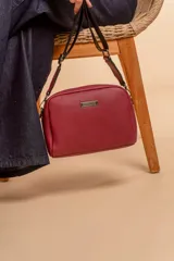 Bandolera pequeña de textura símil cuero color caramelo/marrón, con dos compartimentos principales con cierre. Correa ancha ajustable de tela negra con inscripción en relieve.