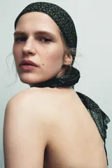 Pañuelo tipo pareo estampado con un patrón geométrico en tonos verde, naranja y negro. Presenta un borde de encaje negro a contraste.