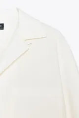 Camisa blanca de algodón con cuello solapa, manga larga con puños abotonados, bolsillo de parche en el pecho, bajo redondeado y cierre frontal con botones.