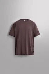 Camiseta marrón de corte relaxed fit, confeccionada en tejido técnico ligero de tacto suave, con cuello redondo y manga corta. Presenta un texto estampado en el delantero y un logo estampado en el bajo.