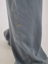 Pantalón gris de tiro medio alto, corte ancho, con bolsillos delanteros y traseros, detalles de atraques y triples costuras en color amarillo.