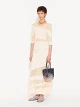 Top ajustado al cuerpo, largo hasta la primera cadera y mangas 3/4. Combina tejido liso color crema con organza transparente en diagonal.