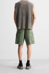 Bermuda color verde militar, de corte relaxed fit, con bolsillos frontales y traseros tipo plaqué, detalle de tira y bolsillo multifunción en la pierna, y bajo irregular.