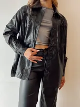 Sobrecamisa oversize de ecocuero negro con flecos en la espalda y tachas plateadas.