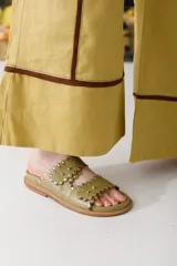 Sandalias bajas color verde oliva con dos tiras con borde festoneado y tachas doradas.