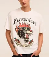 Remera color crema de corte recto, con cuello redondo y mangas cortas. Presenta un estampado estilo tatuaje con un felino en llamas y la frase "Redención es una virtud".