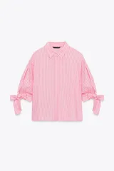 Camisa de lino a rayas verticales rosas y blancas, con cuello solapa, manga corta abullonada y lazos en los puños. Cierre frontal con botones ocultos.