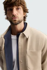 Sobrecamisa negra de tejido con elasticidad, cuello solapa, manga larga con puño abotonado, bolsillos de plastrón en el pecho y cierre frontal con botones a presión.