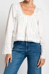 Blusa blanca de algodón con escote en U y mangas largas acampanadas. Presenta detalles de encaje en el escote, el frente y los puños.