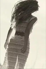 Vestido largo blanco de puntilla de algodón con flecos, corte recto y escote asimétrico. Incluye cinturón de cuero marrón con apliques metálicos.